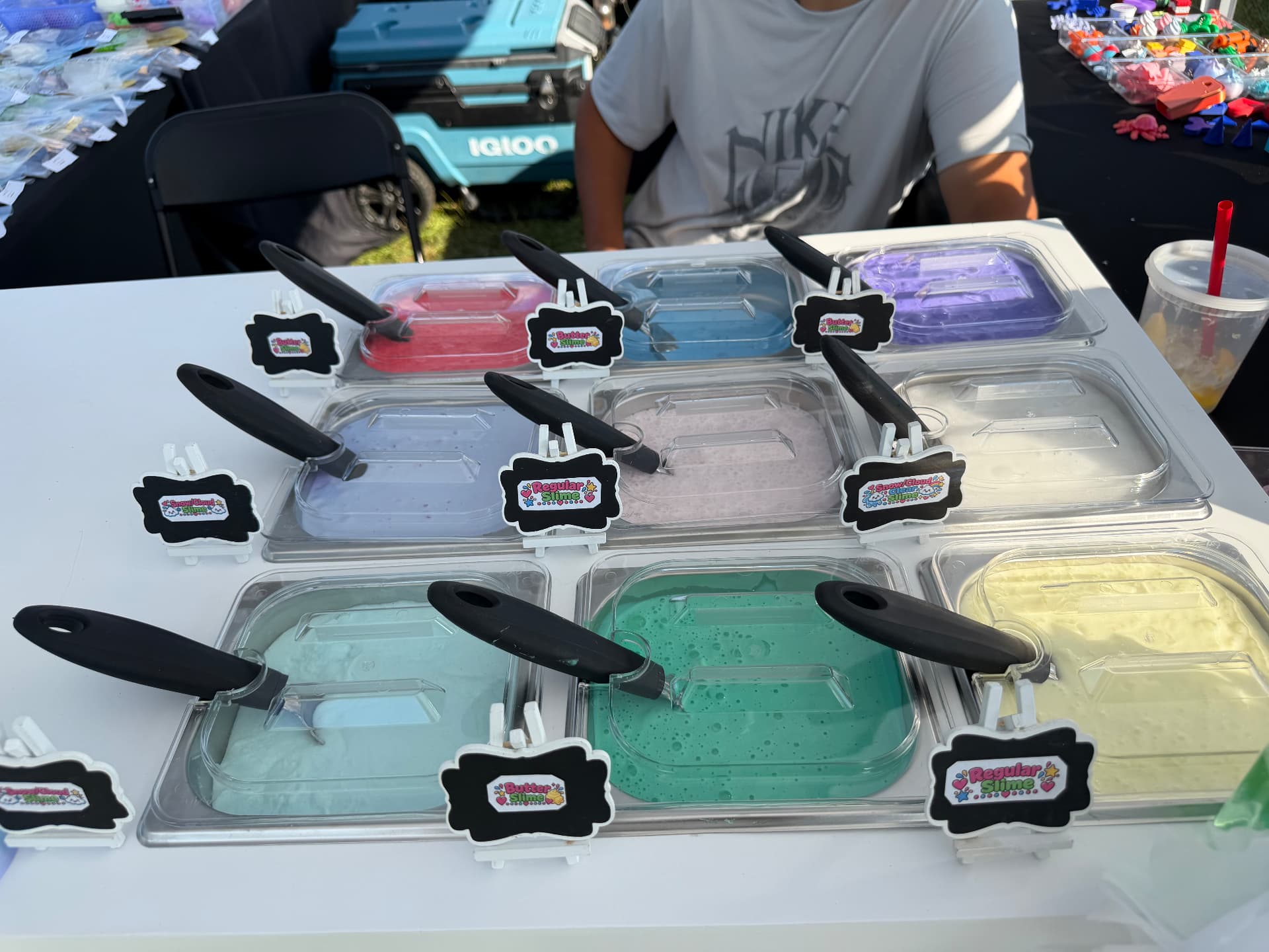 Trays of butter slime, snow cloud slime and regular slime in bright colors with labeled signs