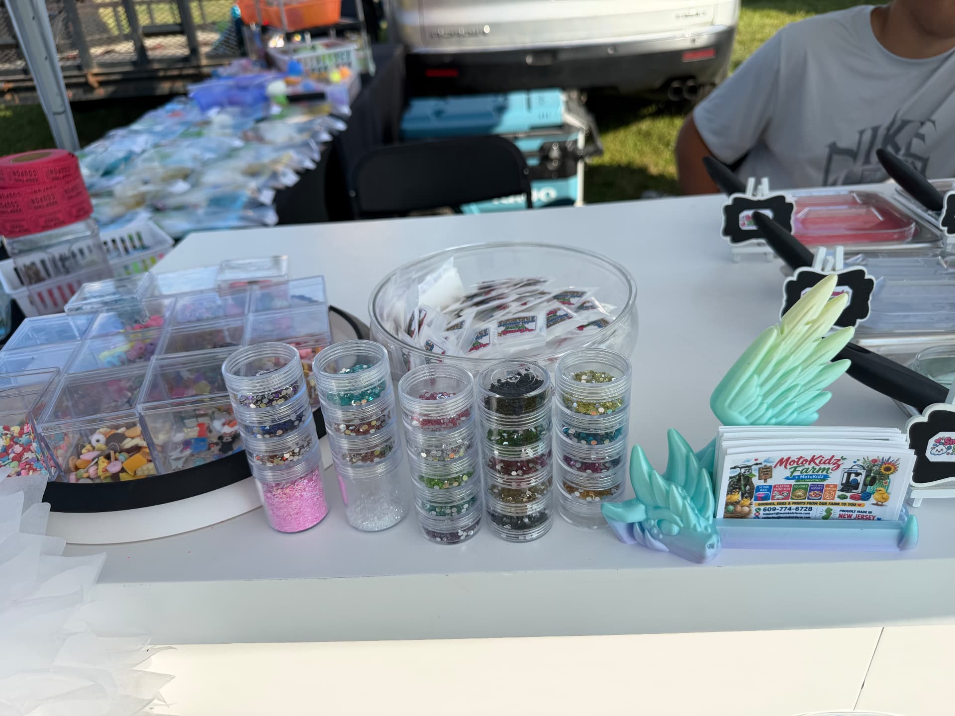 Jars of glitter and rhinestones with clay charms and MotoKidz Farm business cards on the slime bar