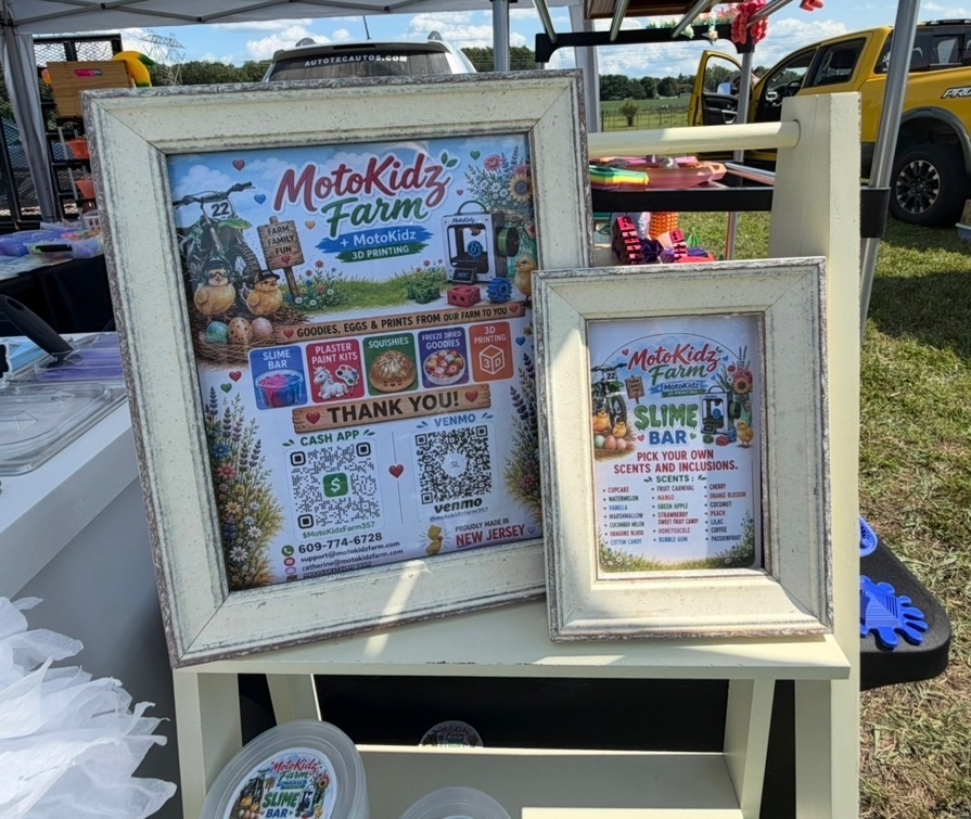 Framed MotoKidz Farm signs listing slime bar scents and inclusions at the event booth